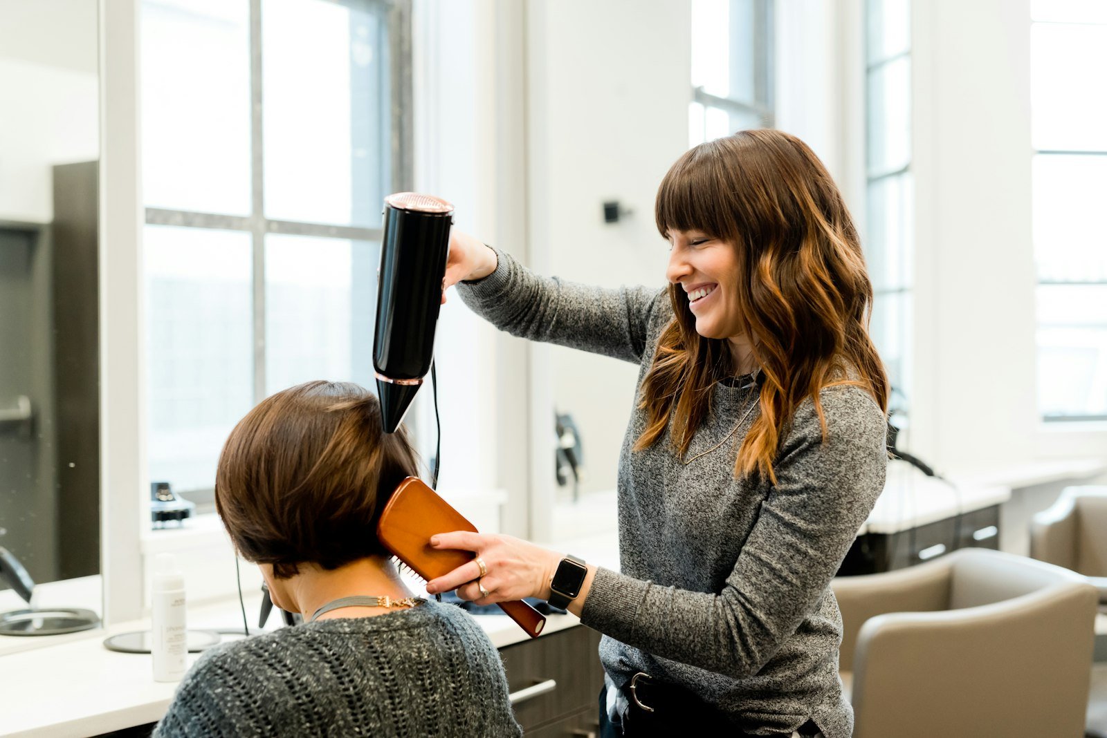 Hairstylist blow-drying a client's hair in a bright, modern studio