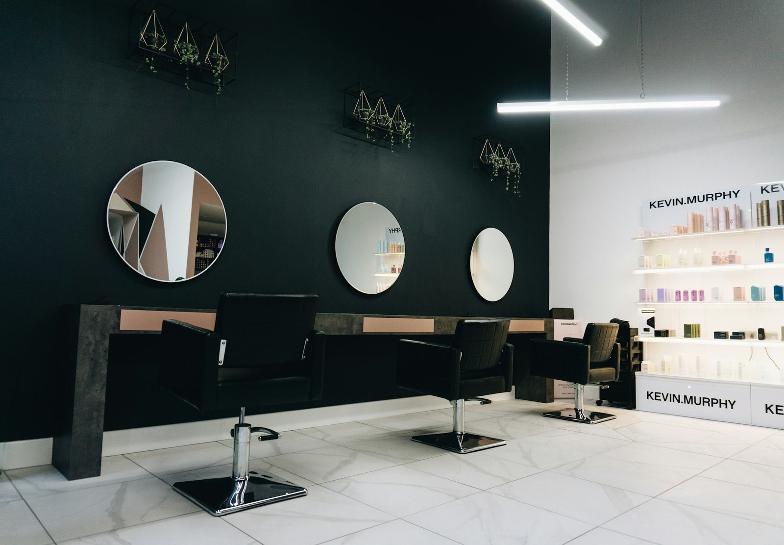 Modern salon interior with round illuminated mirrors and a dark feature wall